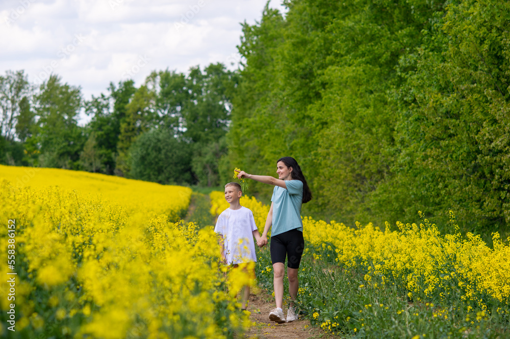 A young mother leads her son into a field with yellow flowers