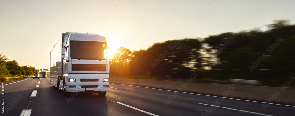 Cargo truck with cargo trailer driving on a highway. White Truck delivers goods in early hours of the Morning - very low angle drive thru close up shot. fast motion blur effect