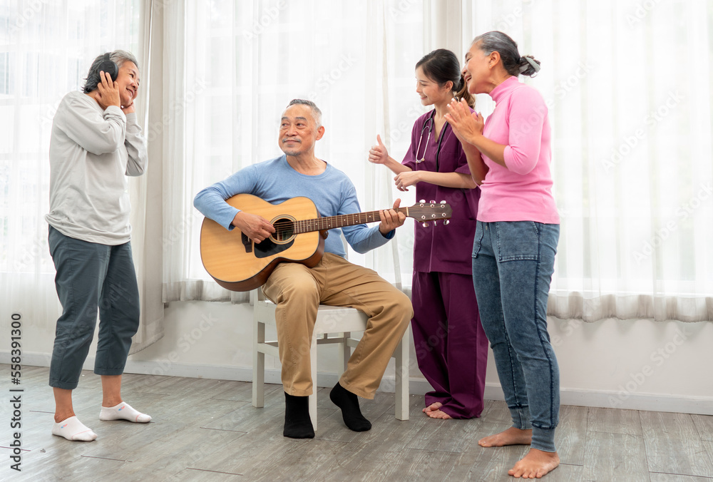 Fototapeta premium Selective focus senior man happy playing acoustic guitar with friends. Elderly male musician sitting at party has fun with cheerful family singing together. Leisure activity of asian grandfather.