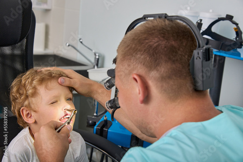 Fotografie When examining a small child, the otolaryngologist uses modern equipment, a headlamp illuminator and a nasal mirror