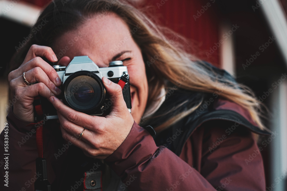 Fototapeta premium Blond woman takes a photo. Girl with long fair hair focuses with an analog camera. Inspiring young creative artist making photo with vintage retro camera.