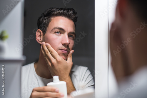 Photos Man is applying aftershave while looking himself in the mirror.