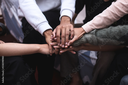 View of diverse senior and young people sitting in circle and putting hands together in community meeting or group therapy session. Concept of support, unity, success, help and trust.