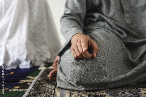 Muslim man praying, sitting in tahiyat position with index finger raised, close-up.