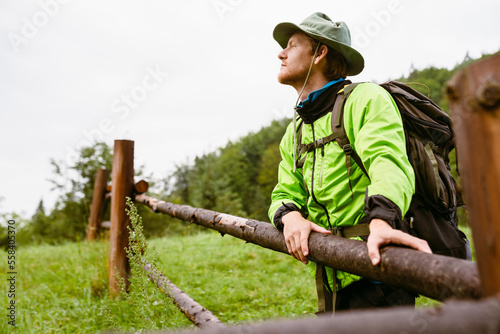 Young man tourist standing near wooden fence during hiking in mountains