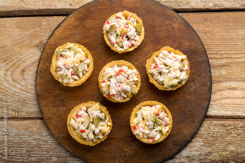 Salad in tartlets with shrimps and pineapple on a round wooden board.