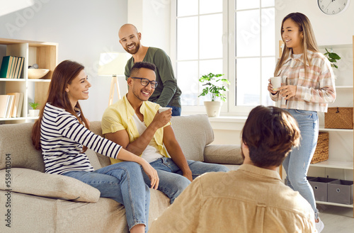 Diverse group of happy, smiling young people having fun at cozy gathering at home. Cheerful mixed race multi ethnic friends sharing funny stories, drinking coffee, and enjoying good time together