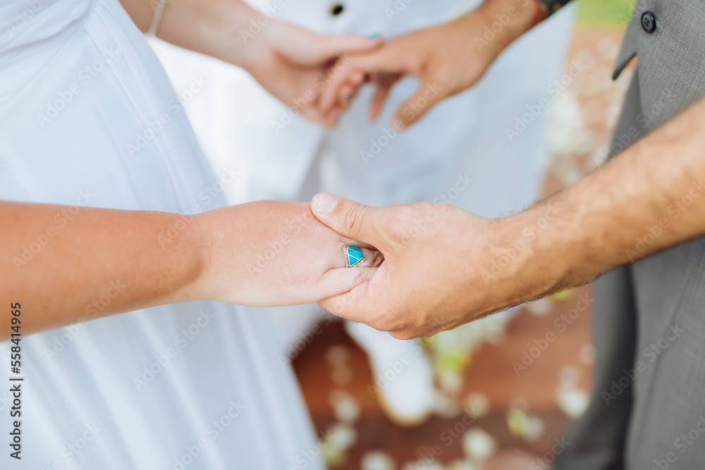 A picture of the bride and groom holding hands at the wedding ceremony. The bride wore a beautiful blue engagement ring at one place. There was a pastor standing as a witness.
