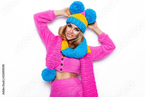 Happy young woman wearing a colorful knitted winter hat, sweater and scarf over white background. Winter fashion.