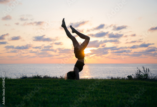Fototapeta Naklejka Na Ścianę i Meble -  young slender girl teenager does handstand at sunset against of sea, beautiful silhouette. concept of cheerfulness, sports education, healthy lifestyle. training with pleasure. soft focus