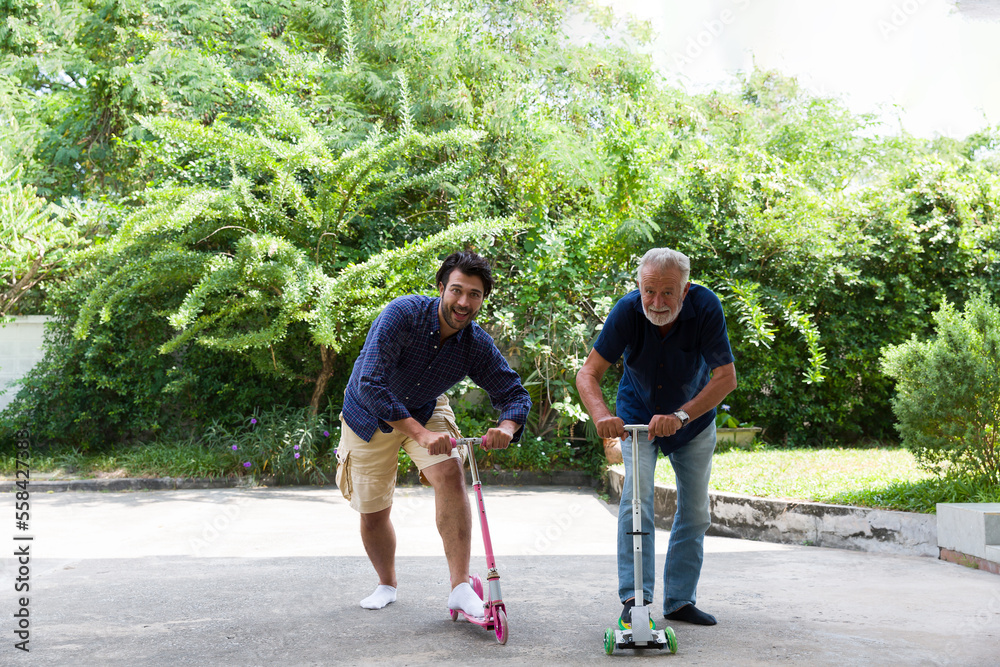 Two men playing scooter together outdoor garden. Elderly man and adult man playing scooter in the backyard. people, family, holiday concept