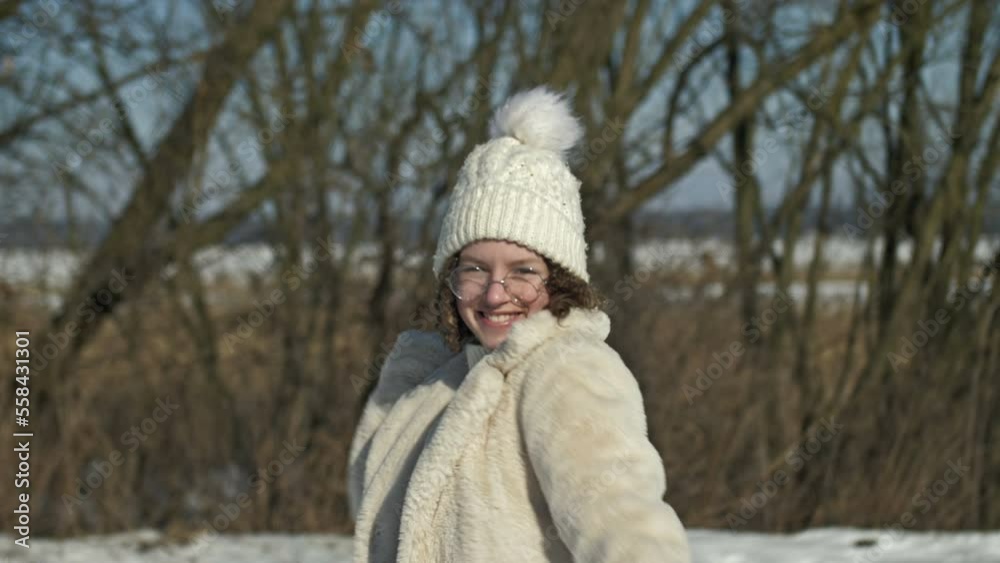 Cheerful teenage girl in a white knitted cap and glasses throws a snowball. Cheerful teenage girl in a white knitted cap and glasses throws a snowball.