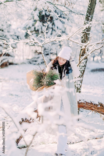 Happy young woman walks in winter forest among trees in sunny day.