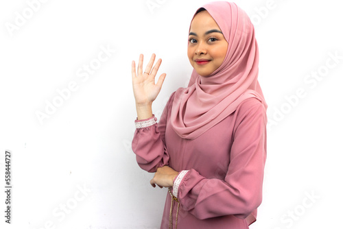 Beautiful asian muslim in hijab looking at camera and wave hand to greeting, isolated on white background