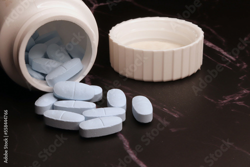 Container with spilled pills on dark background
