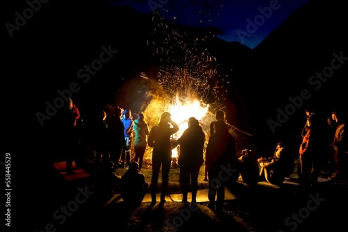 Altyn Arashan Valley, Kyrgyzstan - circa August 2022:  Group of people standing by huge campfire in mountains at night photo