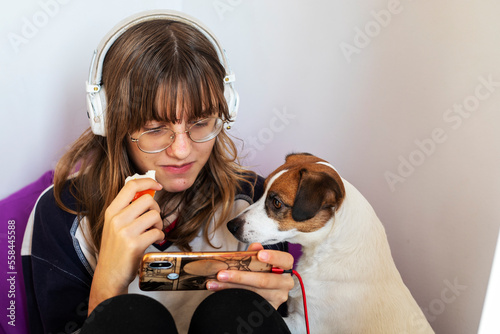 Teenage girl in glasses in headphones and gadgets with a jack russell terrier.