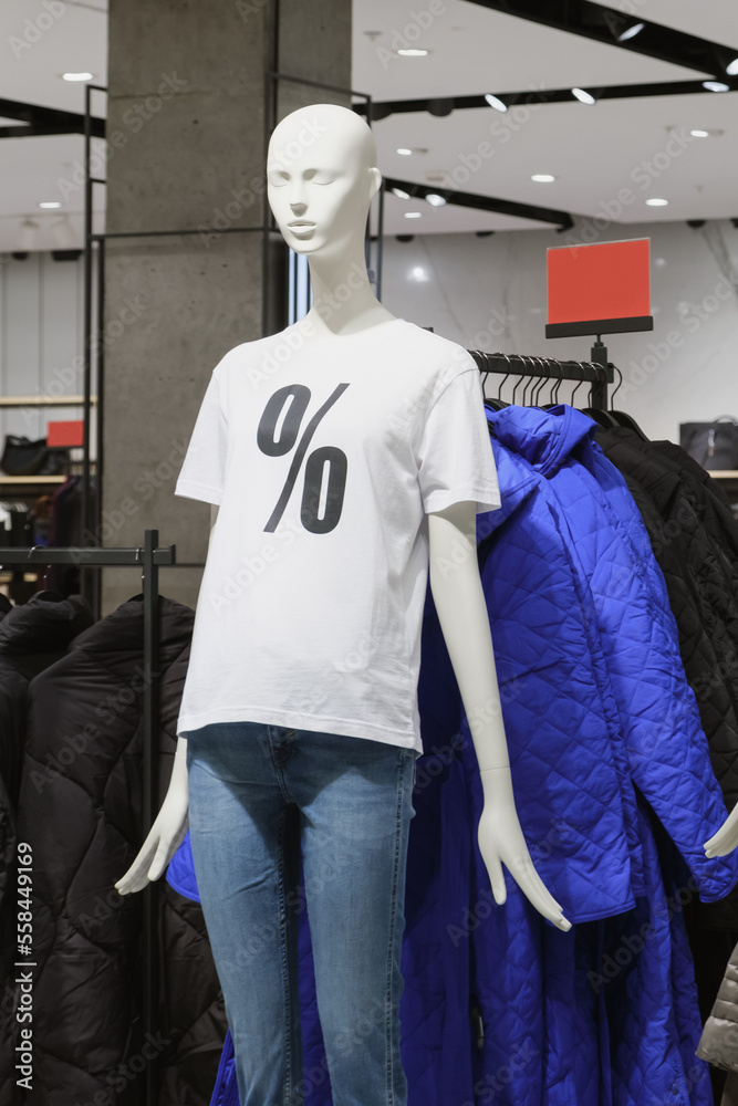White plastic female mannequin in a white T-shirt with a percent symbol and jeans. Decoration of the trading floor of a casual clothing store for seasonal sales. White plastic female mannequin in a white T-shirt with a percent symbol and jeans. Decoration of the trading floor of a casual clothing store for seasonal sales.