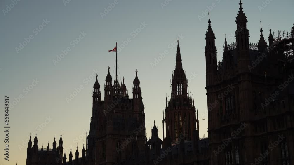 4K video with the national flag of the United Kingdom waving on top of Westminster Palace silhouette during a sunset in London.