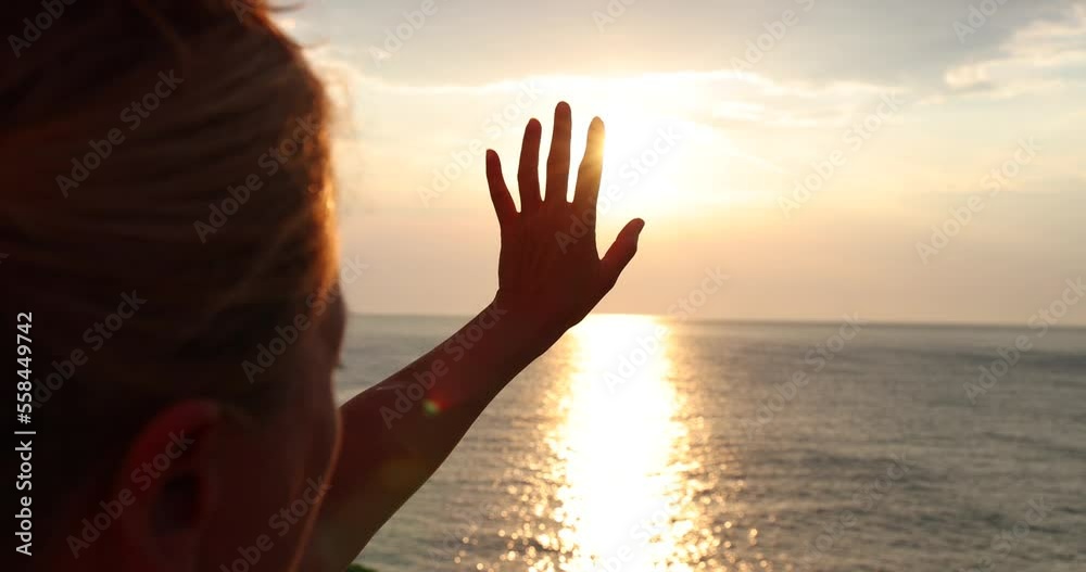 Female hand touching the sun, sunlight passing through fingers at sunset on the sea, closeup shining sun and the sea vacation, season travel nature idyllic.