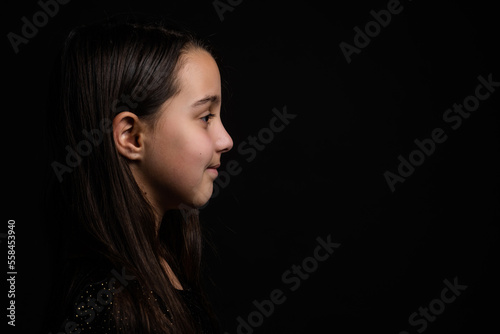 Profile side view face brown-haired little girl standing isolated on black studio background