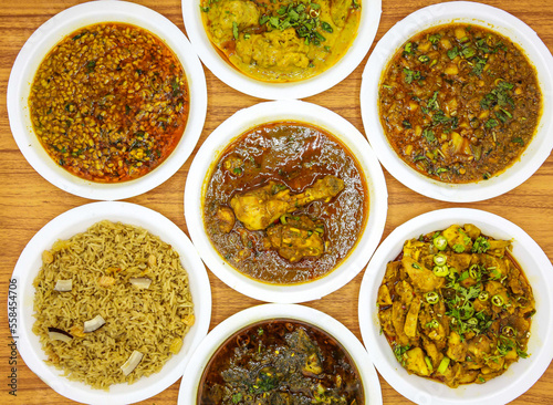 Assorted indian and pakistani spicy food chicken korma, daal mash fry, aloo matar qeema, gobhi gosht, aloo palak and gur chawal served in plate isolated on table top view photo