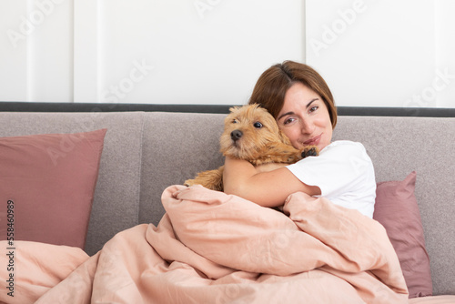 Young and beautiful woman lying in the bed and hugging her adorable pet dog. Perfect friendship concept 