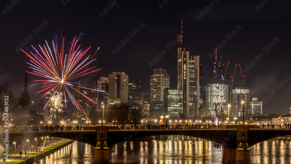 Naklejka premium New years eve with fireworks above the skyline of Frankfurt - Main at night at a cold day in winter with colorful reflections in the water.