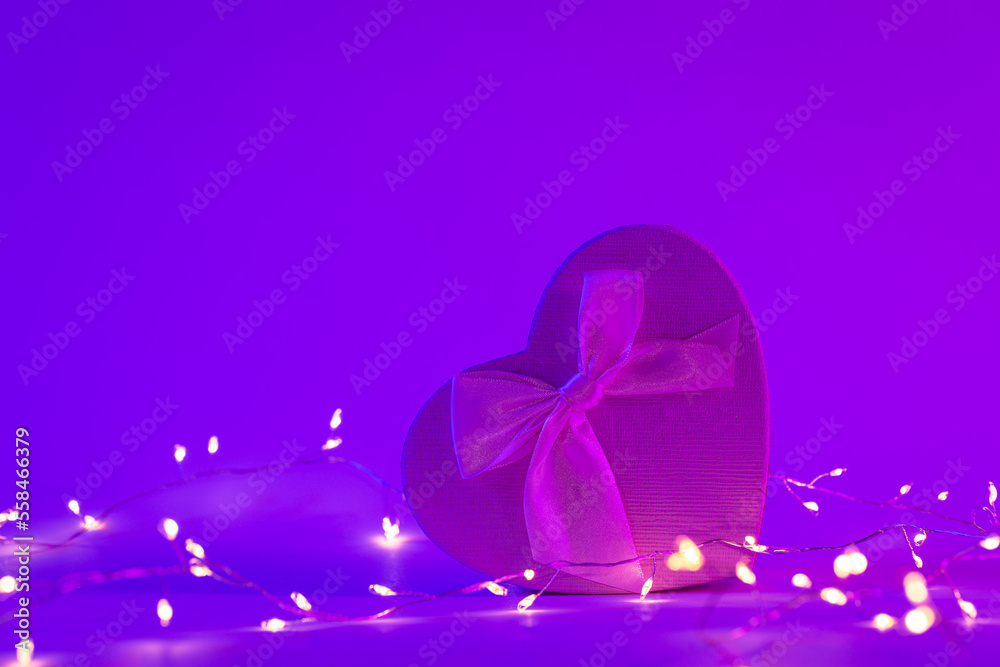 Gift box in the shape of a heart in neon lighting and a garland, the concept of Valentine's day, romance and love, copy space.