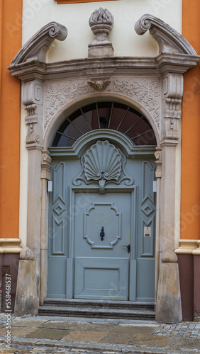 Elegant old doors adorned with intricate details in a decorated façade of a historical significant building, well-maintained, showing the craftsmanship of the ornate carvings and moldings. © Aleks