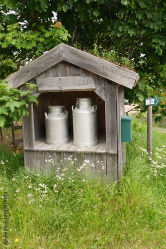 Milchkanne in einem Unterstand aus Holz mit Briefkasten an einem Bauernhof in der Nähe von Hamar, Norwegen. Gesehen am Pilgerweg St. Olavsweg, Gudbrandsdalsleden.