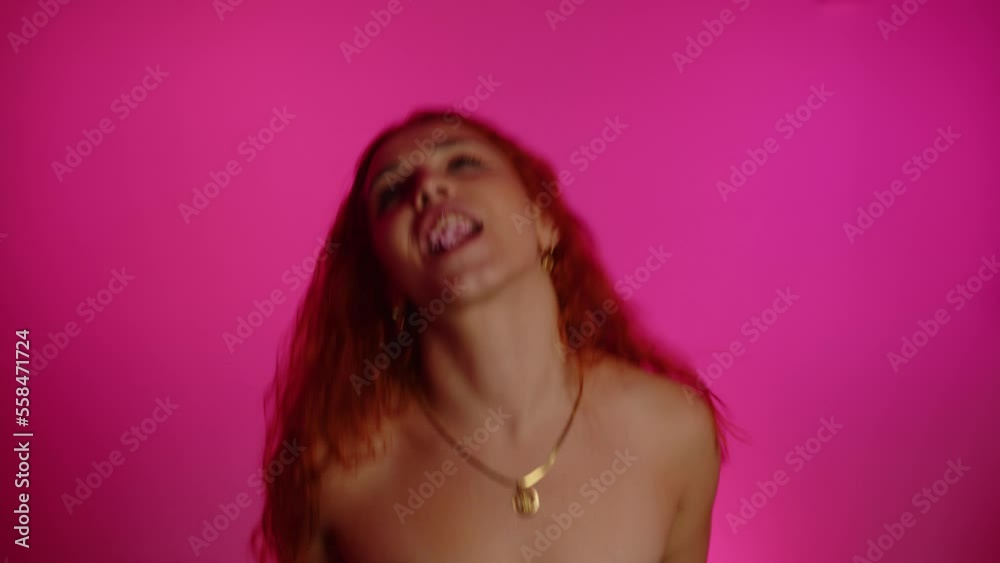 Playful young woman blowing gum, laughing, dancing against pink background