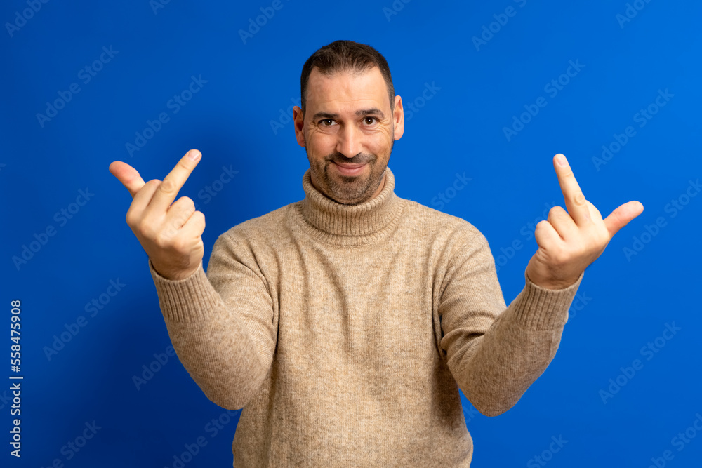 Naklejka premium Hispanic man standing over blue background showing middle finger making fuck you bad expression, provocation and rude attitude.