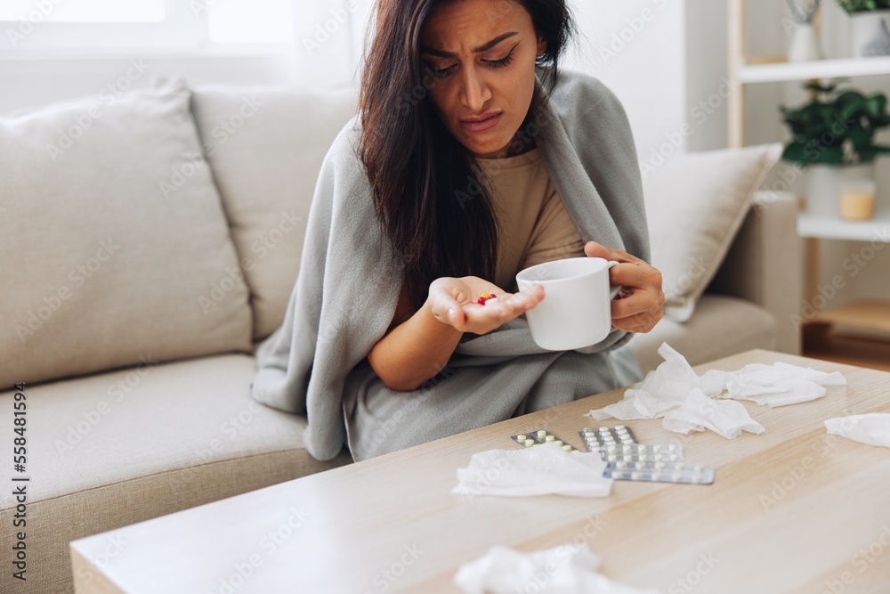 A woman with a cold with pills is treated at home chooses which drugs to take and self-medicates, checks the expiration date while sitting on the couch at home A woman with a cold with pills is treated at home chooses which drugs to take and self-medicates, checks the expiration date while sitting on the couch at home