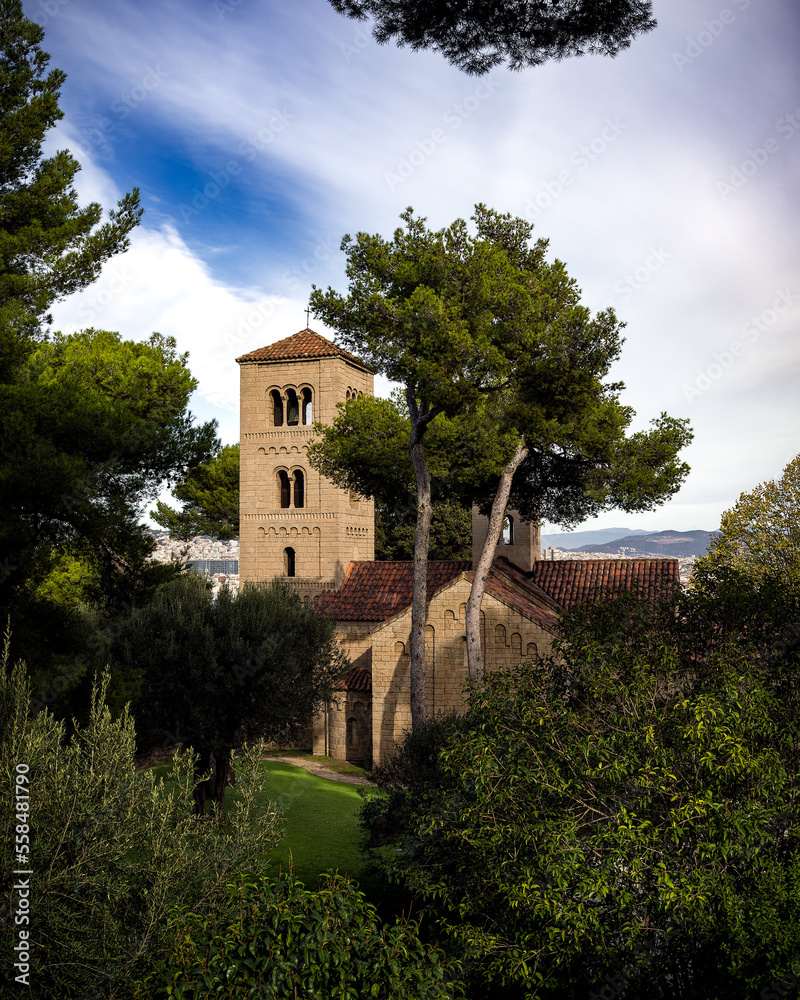Pictoresc church of Sant Miquel in Poble Espanyol surrounded by rich green trees