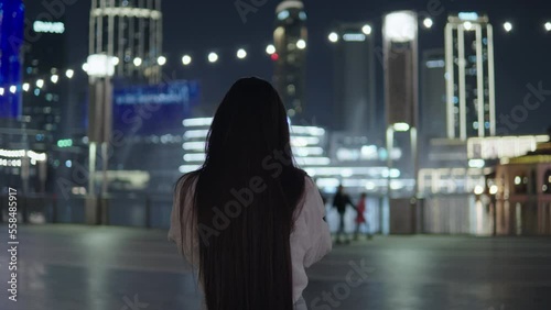 Beautiful leady with long hair shoots a game of singing fountains on a smartphone. A girl at Night city. Glowing multi-colored lanterns and lamps. photo