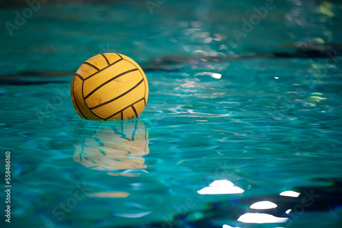 Yellow water polo ball in a swimming pool on blue water background. Film noise and gain