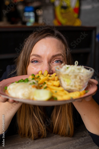 Cheerful woman gesturing hold in hands plate with fries, chicken fillet and vegetable salad. Serving of main dish and garnish closeup, selective focus on human. Love food, restaurant dish, meal photo