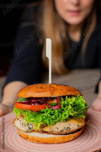 Closeup plate with juicy appetizing chicken burger isolated on waiter background  selective focus. Serving of big caloric sandwich on skewer. Like fast food  self service  restaurant dish  dinner