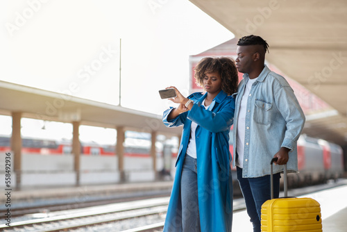 Black couple waiting for train arrival on platform at railway station