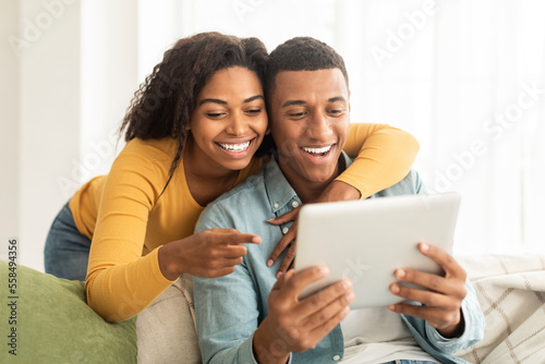 Cheerful millennial african american lady hug guy, looking at tablet, have video call, use app