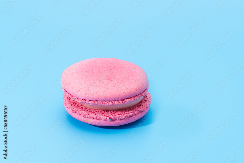 Pink french macaroon or macaron on blue background. Tasty colourful macarons. Cookie made of two smooth halves, fastened with stringy fillings. French pastry made from egg whites.