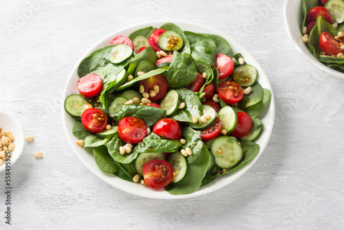 Plate with salad of fresh spinach leaves, cucumbers, cherry tomatoes and pine nuts with dressing on a light gray background. delicious healthy food