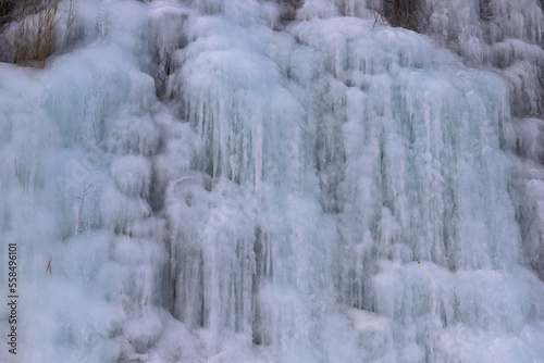 Beautiful ice structures of a frozen waterfall, pretty icicles forming an interesting pattern on a dark rock, creating a cold and moody atmosphere in an ice cave in the mountains