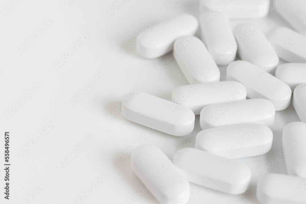 close up macro of scattered white oblong tablet pills on a white background with copy space