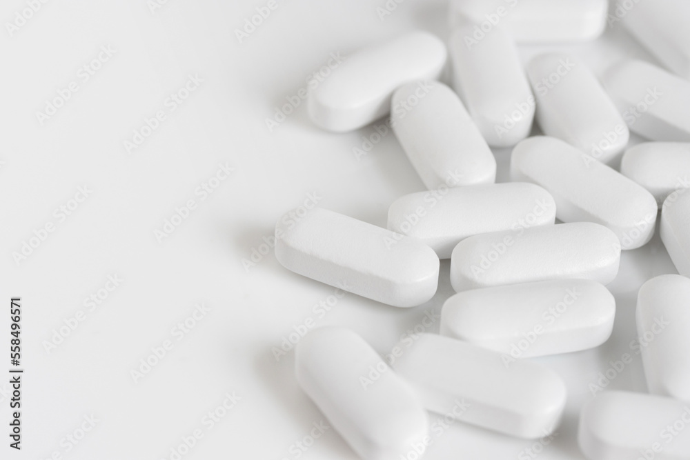 close up macro of scattered white oblong tablet pills on a white background with copy space close up macro of scattered white oblong tablet pills on a white background with copy space