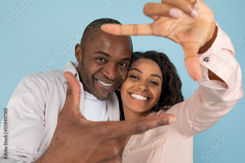 Capturing moments. Close up portrait of black couple making picture frame with fingers, looking at camera and smiling