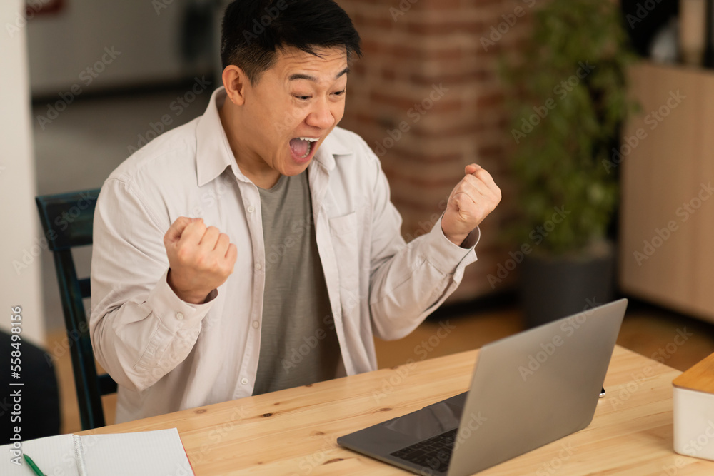 Overjoyed asian mature male entrepreneur using laptop, shouting and gesturing yes, sitting at workplace at home Overjoyed asian mature male entrepreneur using laptop, shouting and gesturing yes, sitting at workplace at home