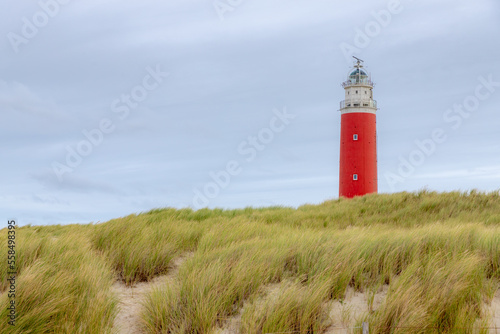 The Eierland Lighthouse on the northernmost top of the Dutch island of Texel, Red lighthouse tower on the sand dunes with european marram grass and cloudy sky as background, North Holland, Netherlands
