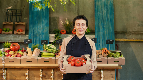 Foto Woman farmer holding box of fresh bio tomatoes at healthy food marketplace, selling homegrown produce